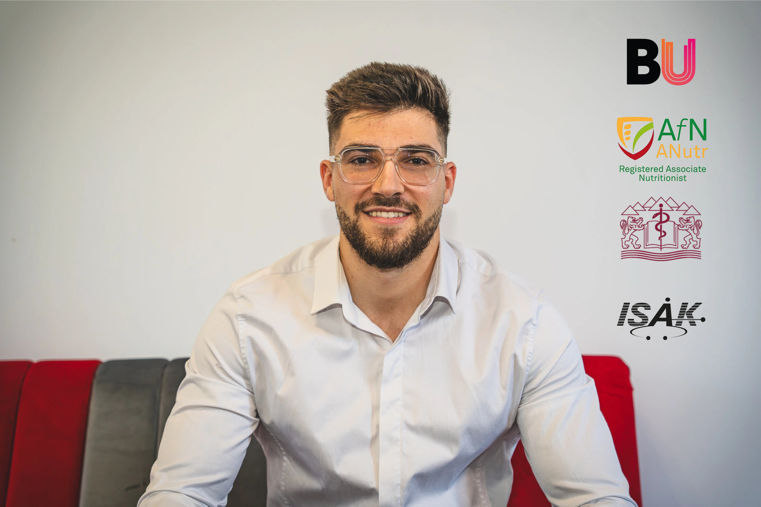 Man sitting on a red couch with logos of institutions behind him